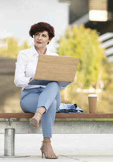 Schöne Geschäftsfrau sitzt mit Laptop auf einer Bank im Büropark - JCCMF04065