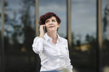 Schöne weibliche Fachkraft, die vor einem Bürogebäude mit einem Mobiltelefon spricht - JCCMF04068