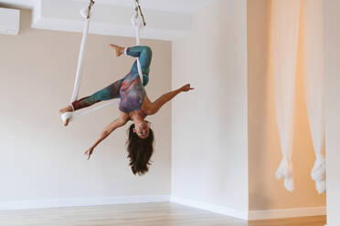 Sportlerin mit ausgestreckten Armen beim Aerial Yoga im Studio - OCAF00772