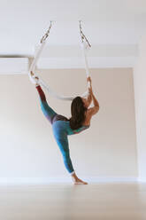 Weibliche Turnerin übt Aerial Yoga im Studio - OCAF00773