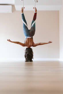 Sportlerin mit Kopf nach unten übt Yoga im Studio - OCAF00776