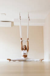 Sportlerin mit Beinspagat übt Aerial Yoga im Studio - OCAF00782