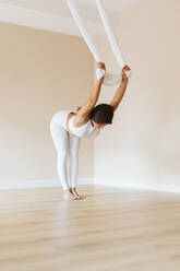 Weibliche Turnerin, die sich beim Üben von Aerial Yoga im Studio beugt - OCAF00783