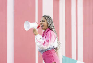 Young woman screaming through megaphone by wall - JCCMF04119