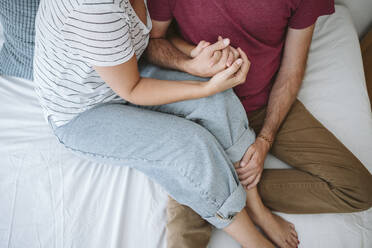 Mid adult couple with hands clasped sitting on bed - EBBF04598