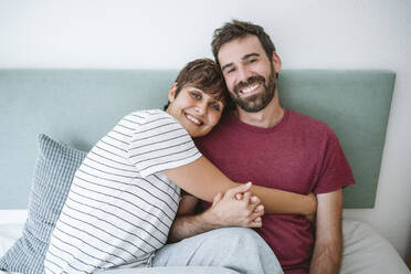Glückliches erwachsenes Paar sitzt zusammen auf dem Bett zu Hause - EBBF04600