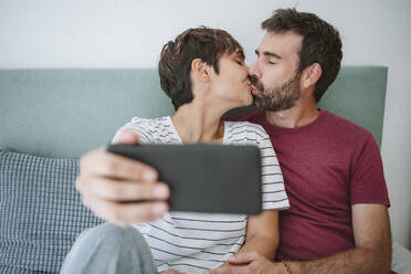 Zärtliches Paar, das sich küsst, während es ein Selfie mit dem Smartphone zu Hause macht - EBBF04606