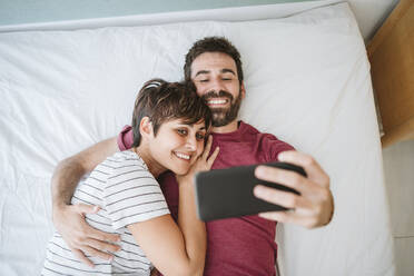 Man with woman taking selfie though smart phone while lying on bed - EBBF04618