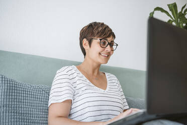 Frau mit Brille benutzt Laptop auf dem Bett zu Hause - EBBF04624