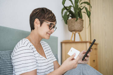 Frau mit Brille, die zu Hause per Online-Banking mit Kreditkarte bezahlt - EBBF04627