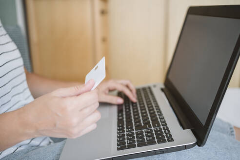 Frau hält Kreditkarte, während sie zu Hause einen Laptop benutzt - EBBF04628