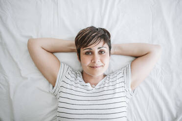 Woman with hands behind head relaxing on bed at home - EBBF04648