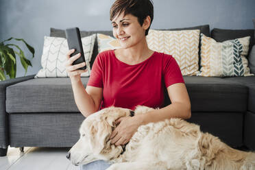 Frau benutzt ihr Smartphone, während sie mit ihrem Golden Retriever zu Hause sitzt - EBBF04651