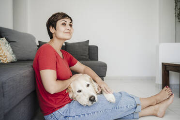 Thoughtful mid adult woman sitting with Golden retriever at home - EBBF04653