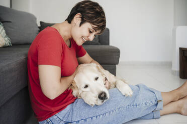 Smiling woman sitting with Golden retriever at home - EBBF04654