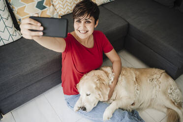 Frau nimmt Selfie mit Hund, während im Wohnzimmer zu Hause sitzen - EBBF04655