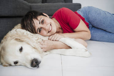 Lächelnde erwachsene Frau mit Hund zu Hause auf dem Boden liegend - EBBF04661