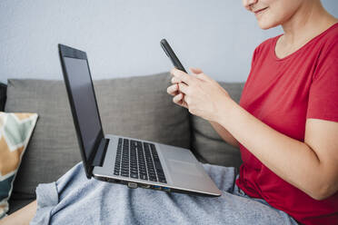 Freiberuflerin mit Laptop und Smartphone auf dem Sofa im Heimbüro - EBBF04668