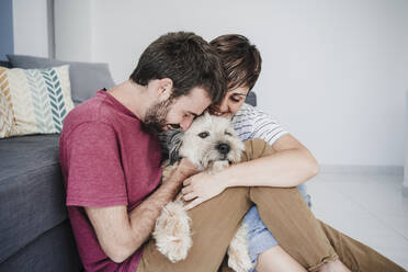 Mid adult couple embracing dog while sitting at home - EBBF04674