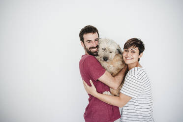 Glückliches mittleres erwachsenes Paar, das einen Hund vor einer Wand hält - EBBF04680