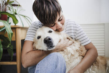 Mid adult woman embracing dog at home - EBBF04708