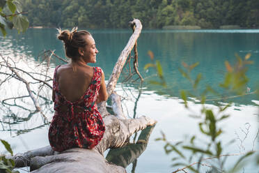 Junge Frau entspannt sich auf einem umgestürzten Baum am Seeufer im Nationalpark Plitvicer Seen - JAQF00831