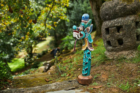 Skulptur eines Drachens mit Ornament auf einer Treppe gegen eine raue Steinlaterne im Garten von Bali Indonesien - ADSF30545