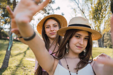 Content female teenagers with outstretched arms interacting while looking at camera on meadow in summer - ADSF30553