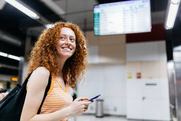 Seitenansicht einer Frau mit Mobiltelefon und Rucksack, die auf dem Bahnsteig der U-Bahn wegschaut - ADSF30573