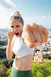 Angry female boxer shouting while showing hitting technique and looking at camera during workout in sunny city - ADSF30599