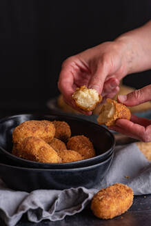 Crop unerkennbar Person demonstriert die Hälfte der leckeren frittierten Krokette mit Käsefüllung auf schwarzem Hintergrund - ADSF30601