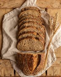 Top view of fresh cereal bread pieces with wheat spikes on creased textile on wooden surface - ADSF30602