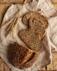 Top view of fresh cereal bread pieces with wheat spikes on creased textile on wooden surface - ADSF30604