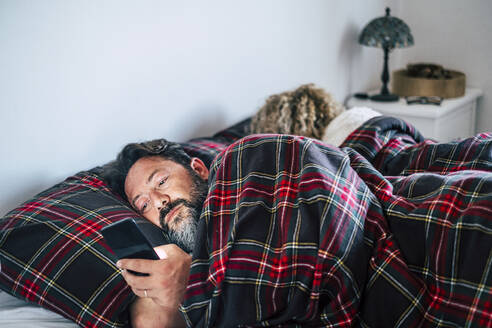 Reifer Mann benutzt Mobiltelefon bei Frau auf Bett - SIPF02468