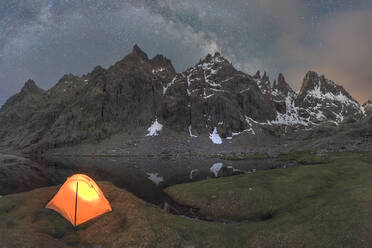 Scenic view of tent on lake shore against snowy mountain under cloudy sky in evening - ADSF30667