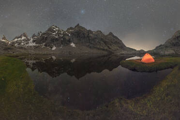 Scenic view of tent on lake shore against snowy mountain under cloudy sky in evening - ADSF30669