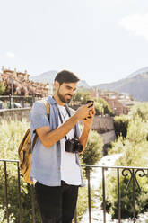 Smiling man photographing through mobile phone by railing - MGRF00502