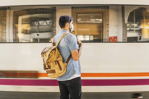 Mann mit Rucksack wartet am Bahnhof auf einen Zug - MGRF00508