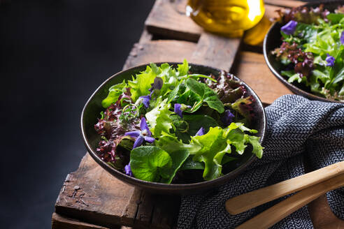 Von oben schmackhafter vegetarischer Salat mit grünen und roten Salatblättern und essbaren Blüten vor einem Krug mit Öl - ADSF30693