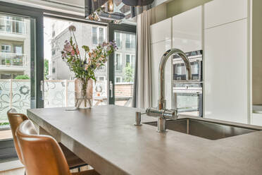 Stilvolles Interieur einer modernen Küche mit weißen Schränken und Geräten und einem Spülbecken über dem Tresen in einem großen Haus mit Glaswand - ADSF30715
