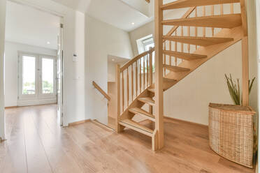 Kreative Gestaltung des Hausinneren mit geschwungener Treppe und Strohkorb auf Holzboden bei Tag - ADSF30745