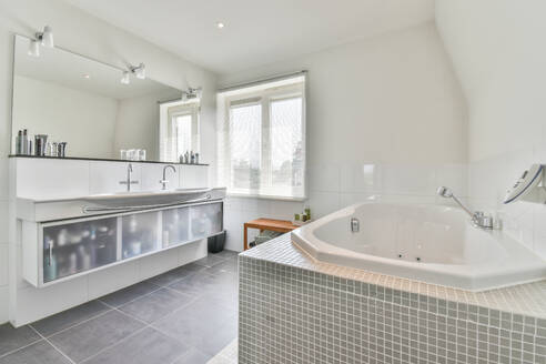 Zeitgenössisches Badezimmerinterieur mit Badewanne gegen Duschkabine und Schönheitsprodukte auf Regal in hellem Haus - ADSF30749