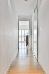 Narrow corridor interior with white walls and wooden floor under lamp at home in daytime - ADSF30755