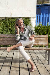 Glücklicher Mann hört Musik über einen drahtlosen Kopfhörer, während er auf einer Bank sitzt - VEGF05072