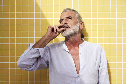 Älterer Mann rauchend vor gelber Wand - VEGF05078