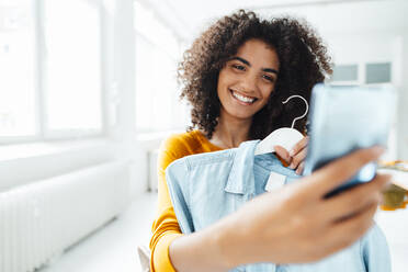 Smiling woman with shirt taking selfie through mobile phone - KNSF09066