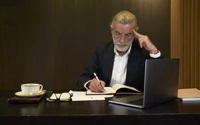 Geschäftsmann schreibt in Tagebuch bei der Arbeit am Schreibtisch im Hotel - VEGF05088