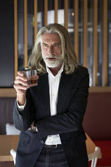 Männlicher Berufstätiger, der ein Whiskeyglas hält, während er in einem Hotelcafé steht - VEGF05094