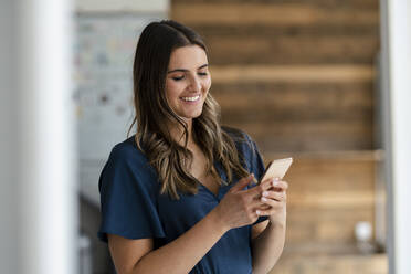 Smiling businesswoman using mobile phone in office - KNSF09090