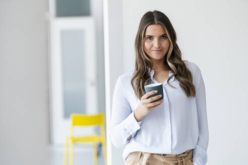 Female business professional holding coffee cup in office - KNSF09148